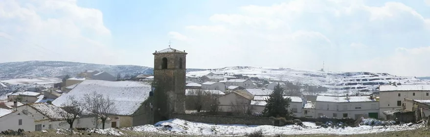 Panorámica de un pueblo cubierto de nieve con torre de iglesia y casas.