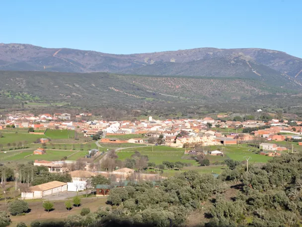 Vista aérea de un pueblo con campos verdes y montañas al fondo.