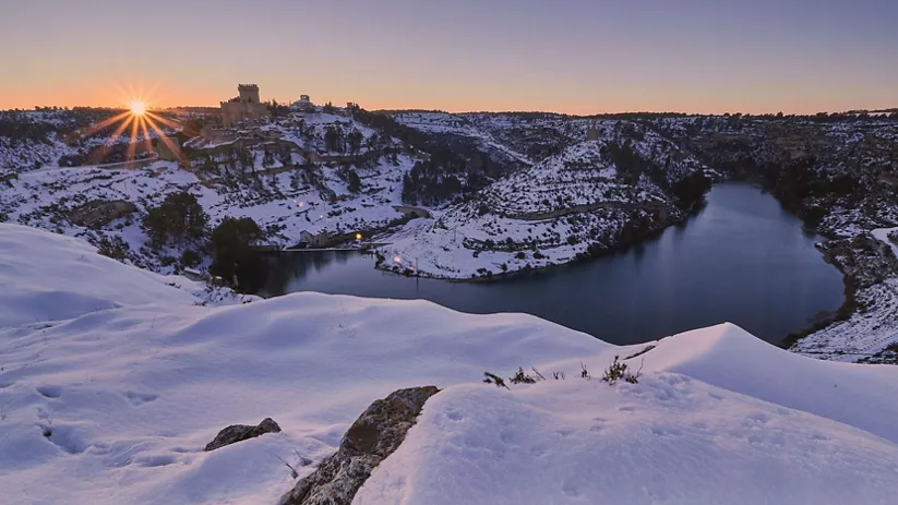 Río entre colinas nevadas al amanecer visto desde un mirador elevado.