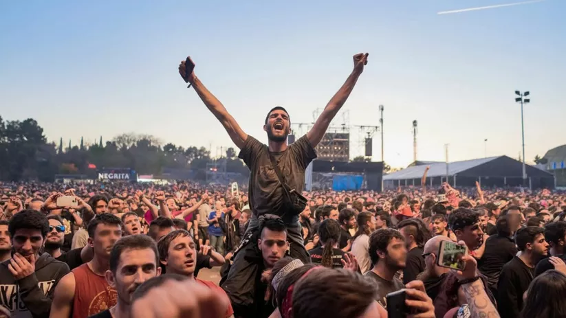 Persona a hombros con los brazos en alto en medio de una multitud durante un concierto al aire libre.