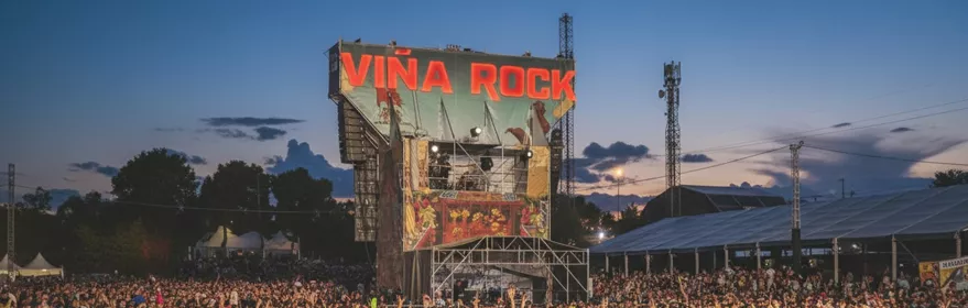 Vista del escenario principal y una gran multitud con las manos levantadas al atardecer.