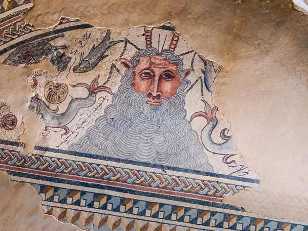 Detalle de mosaico antiguo con figura barbada rodeada de decoración geométrica.