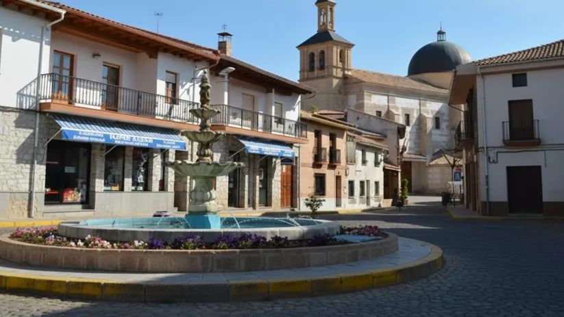 Una fuente central circular de niveles en el centro de una plaza adoquinada frente a una iglesia de piedra.