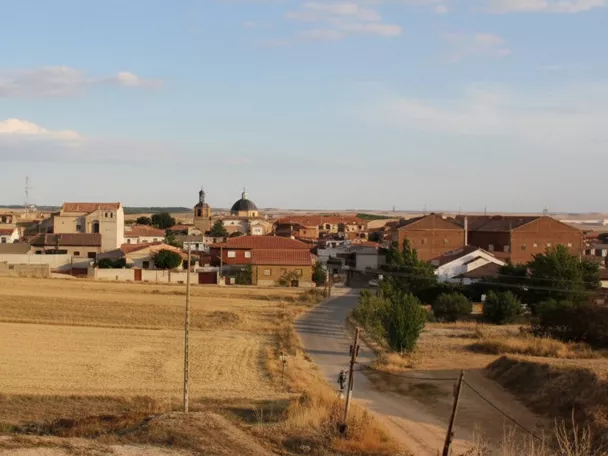 Una vista panorámica a nivel de los ojos de un pueblo rural enclavado detrás de un vasto campo de heno dorado.