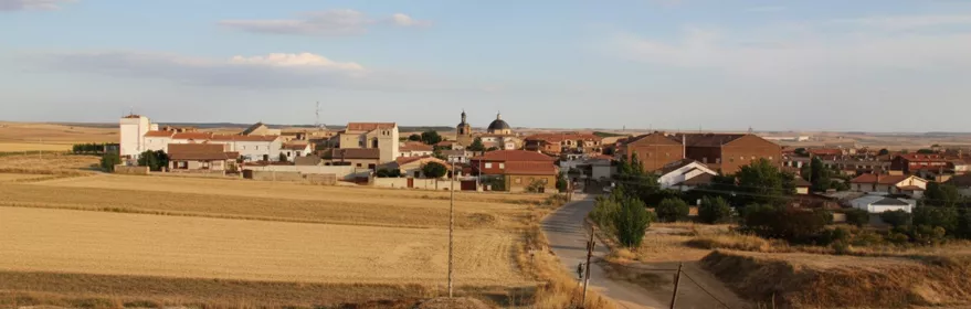 Una vista panorámica a nivel de los ojos de un pueblo rural enclavado detrás de un vasto campo de heno dorado.