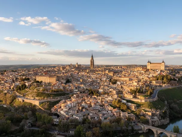 Vista elevada de una ciudad compacta con edificios de piedra y tejados de terracota, situada sobre una colina que serpentea alrededor de un río.
