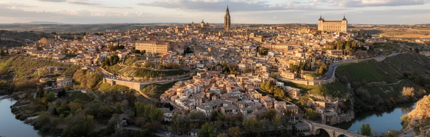 Vista elevada de una ciudad compacta con edificios de piedra y tejados de terracota, situada sobre una colina que serpentea alrededor de un río.