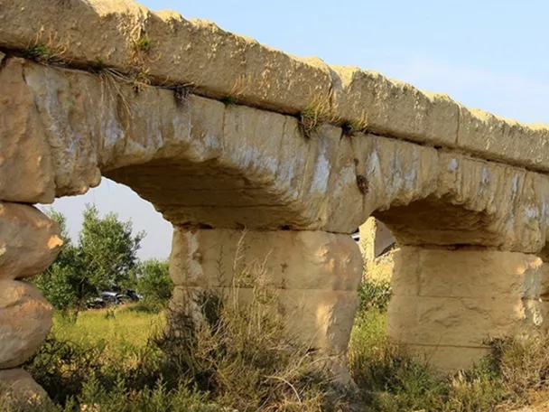 Estructura de piedra con arcos en un entorno natural y vegetación baja.