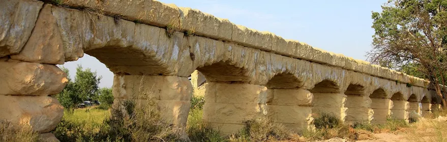 Estructura de piedra con arcos en un entorno natural y vegetación baja.