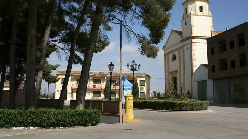 Plaza tranquila con iglesia, árboles altos y buzón amarillo