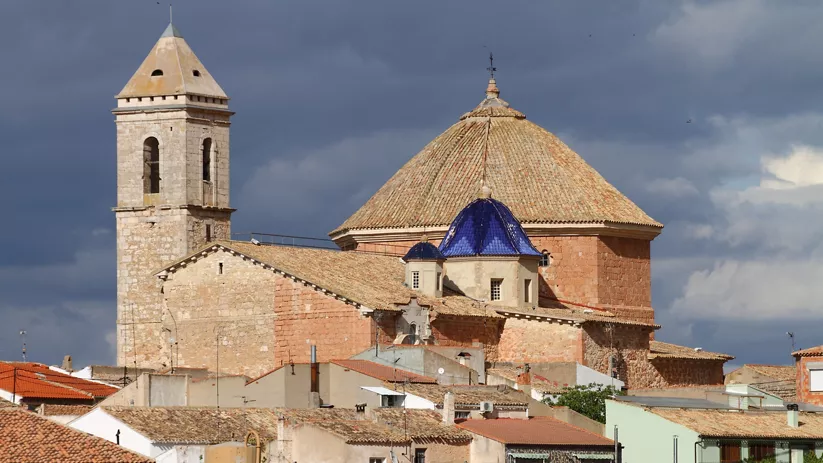 Iglesia de piedra con torre y cúpula entre tejados de casas