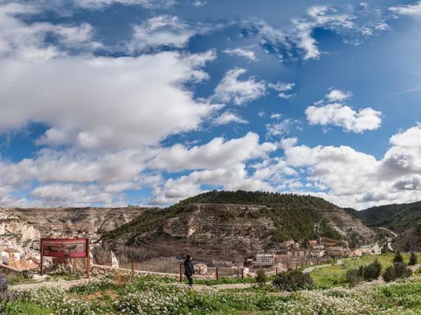 Torre de piedra sobre colina con valle verde y cielo parcialmente nublado.