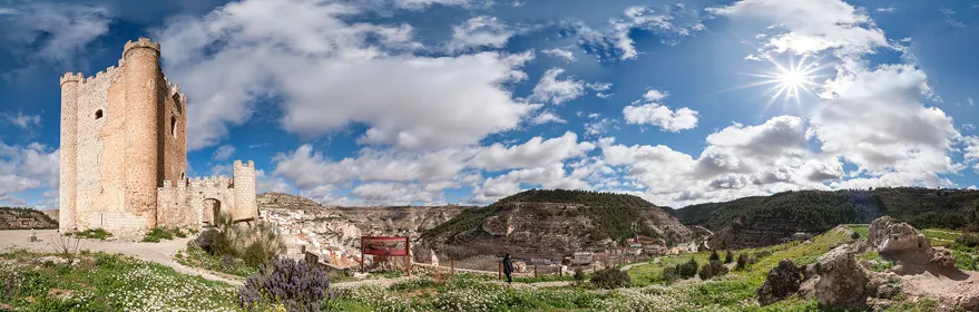 Torre de piedra sobre colina con valle verde y cielo parcialmente nublado.