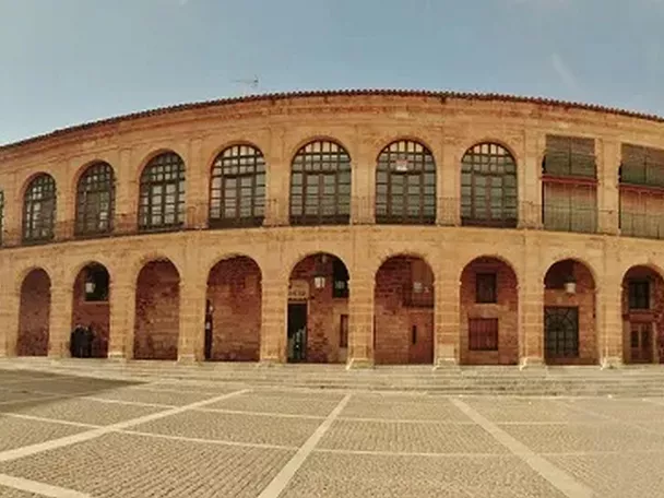 Plaza amplia con edificio porticado de piedra y arcos en dos alturas.