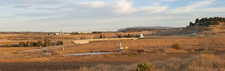 Paisaje de campos secos con carretera, colinas y aerogeneradores