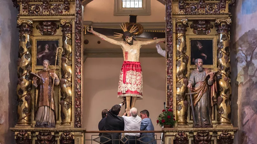 Retablo barroco con escultura central y varias personas alrededor