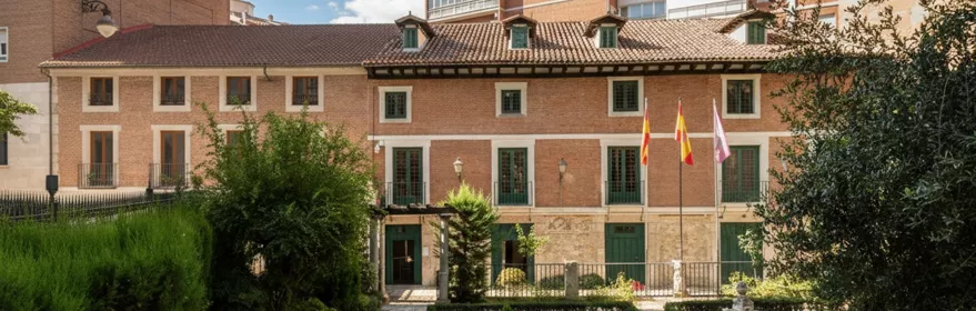 Jardín cuidado con senderos de piedra, fuente circular y edificio histórico al fondo.