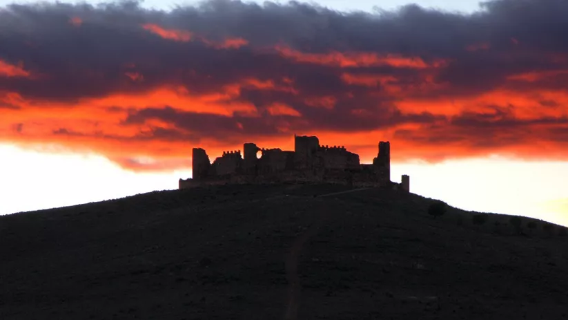Silencio de una fortaleza en ruinas recortada contra un cielo rojizo al atardecer.