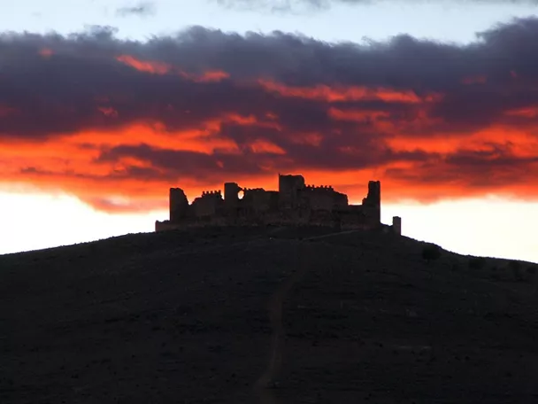 Silencio de una fortaleza en ruinas recortada contra un cielo rojizo al atardecer.