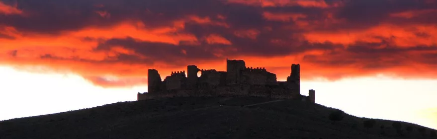 Silencio de una fortaleza en ruinas recortada contra un cielo rojizo al atardecer.