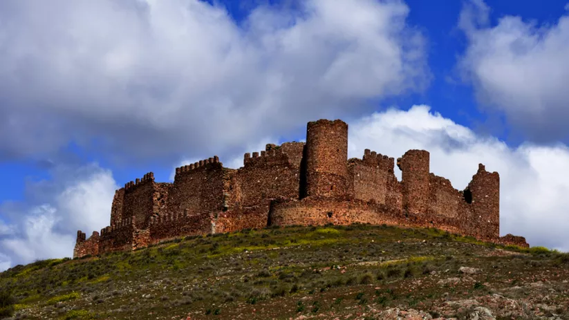 Fortaleza medieval de piedra sobre una colina bajo cielo parcialmente nublado.