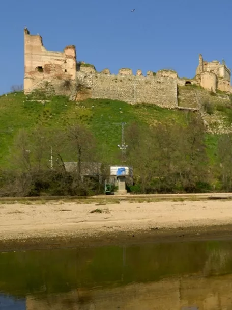 Fortaleza amurallada sobre colina verde reflejada en un río