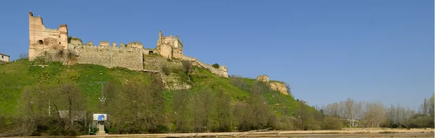 Fortaleza amurallada sobre colina verde reflejada en un río
