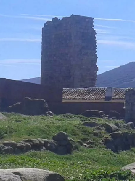 Torre de piedra en ruinas junto a edificaciones rurales y colinas al fondo.