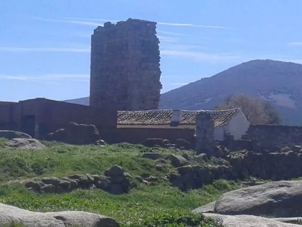 Torre de piedra en ruinas junto a edificaciones rurales y colinas al fondo.