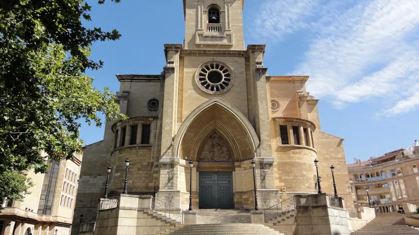 Vista frontal de templo histórico con torre, rosetón y escalinata bajo cielo azul.