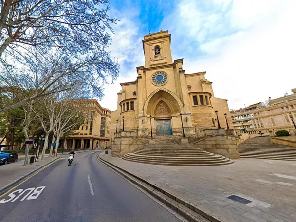 Vista panorámica diurna de una iglesia de piedra con escalinata amplia y calle en primer plano.