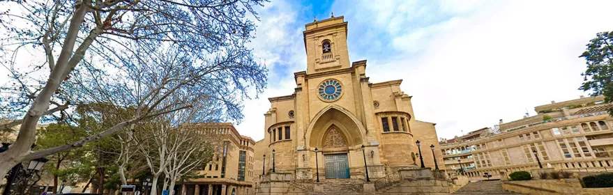 Vista panorámica diurna de una iglesia de piedra con escalinata amplia y calle en primer plano.