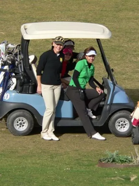 Imagen de un carro de golf en el campo con un grupo de golfistas