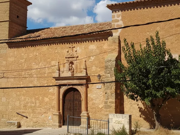 Fachada lateral de iglesia de piedra con portada y árbol
