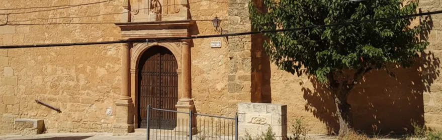 Fachada lateral de iglesia de piedra con portada y árbol