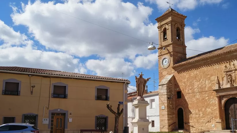 Plaza con estatua, iglesia de piedra y torre con reloj