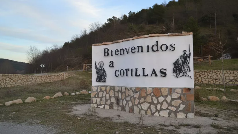 Cartel de bienvenida junto a carretera y ladera boscosa