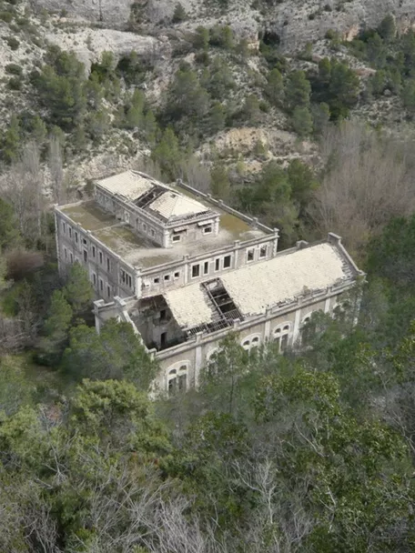 Edificio abandonado rodeado de bosque visto desde una ladera rocosa.