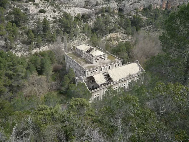 Edificio abandonado rodeado de bosque visto desde una ladera rocosa.