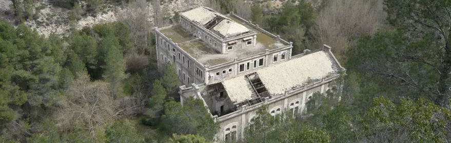Edificio abandonado rodeado de bosque visto desde una ladera rocosa.