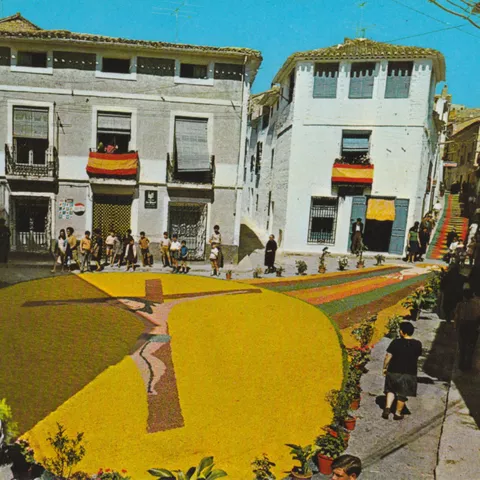 Imagen de una alfombra con una cruz en la calle con gente alrededor