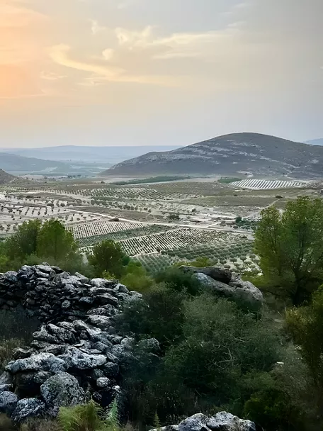 Paisaje rocoso al atardecer con colinas y campos de cultivo