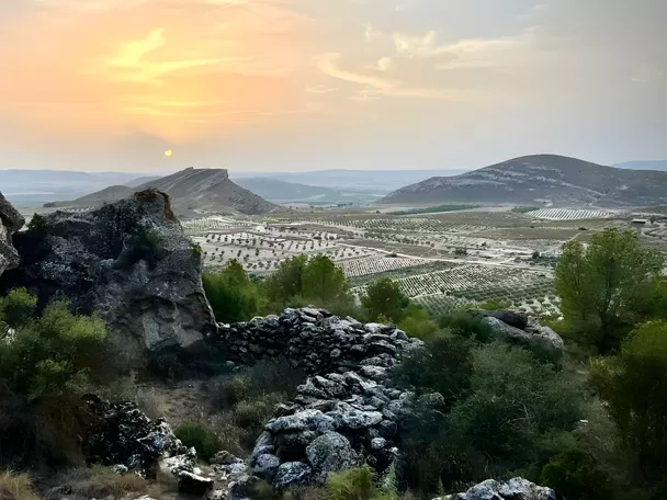 Paisaje rocoso al atardecer con colinas y campos de cultivo