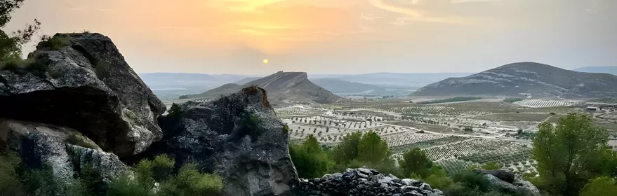 Paisaje rocoso al atardecer con colinas y campos de cultivo