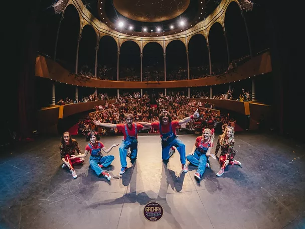 Grupo de intérpretes saludando al público desde el escenario de un teatro lleno.