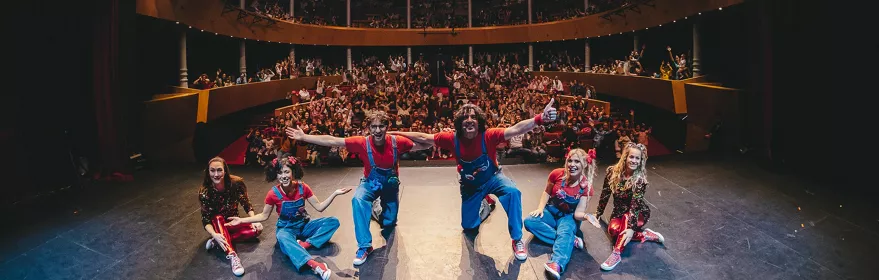Grupo de intérpretes saludando al público desde el escenario de un teatro lleno.