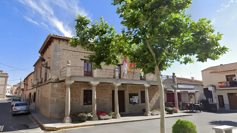 Casa consistorial de piedra con soportales y banderas en la plaza