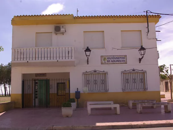 Fachada de edificio consistorial blanco con bancos y faroles