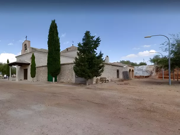 Ermita de piedra en explanada de tierra con cipreses