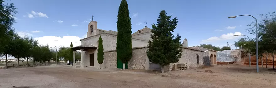 Ermita de piedra en explanada de tierra con cipreses